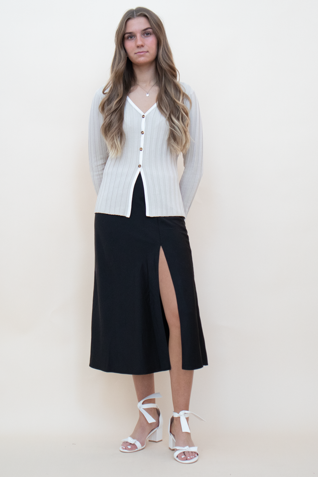 beige knit long sleeve button up, styled with a black silk skirt and a white heel with bows