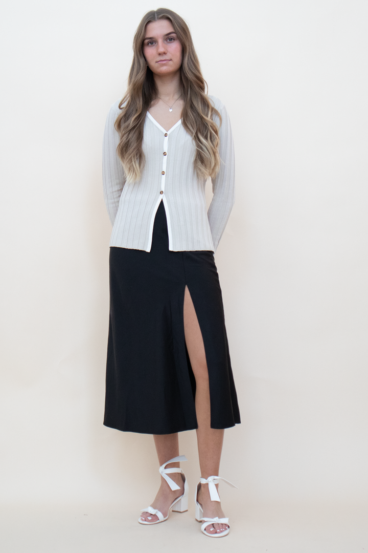 beige knit long sleeve button up, styled with a black silk skirt and a white heel with bows