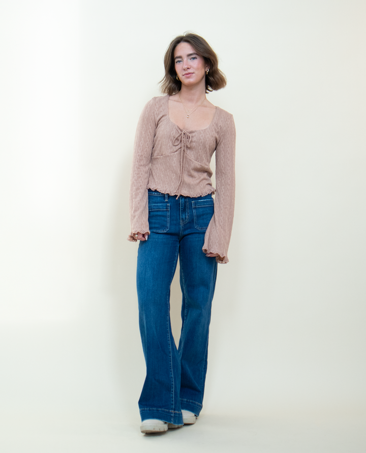 Full length view of dusty pink bell sleeve crop top with front tie and lace hem detail, styled with wide leg blue jeans and white platform shoes