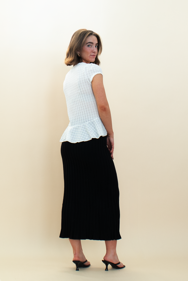 Back view of woman wearing a white textured peplum blouse and black ribbed knit midi skirt, styled with black kitten heels from Groove Closet.
