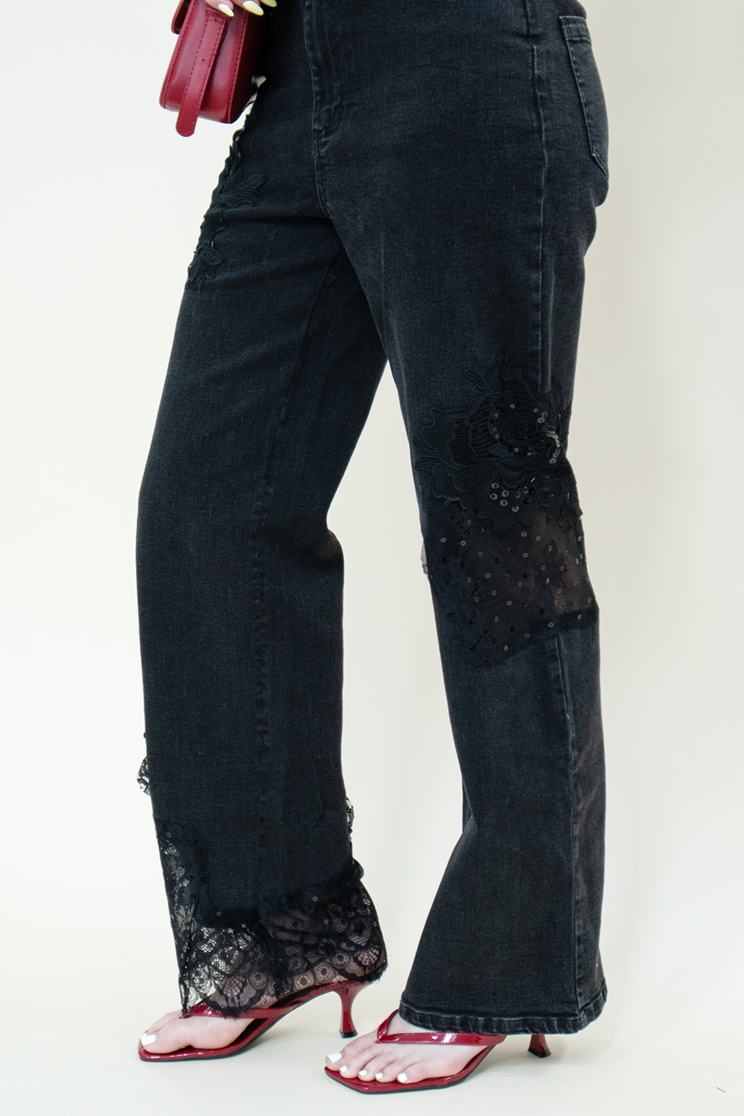 Detailed view of black straight-leg jeans with floral lace inserts from Groove Closet, paired with a polka dot lace-trim camisole, black belt, red kitten heels, and a red shoulder bag.