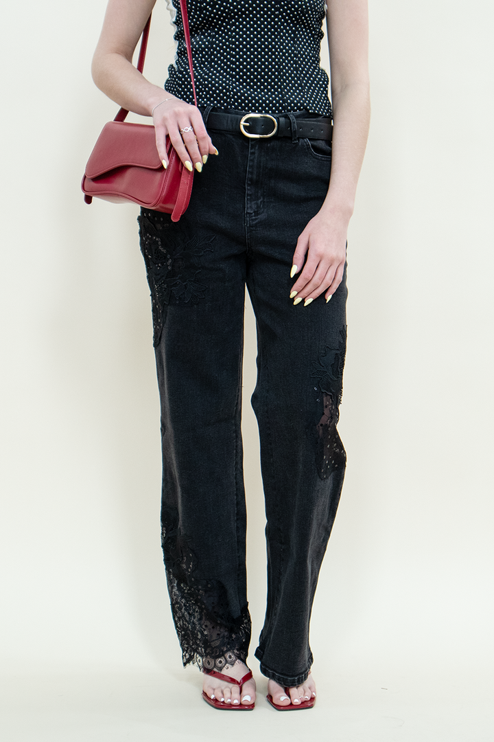 Close-up of black straight-leg jeans with sheer floral lace detailing at the knees and hem, paired with red kitten heels.