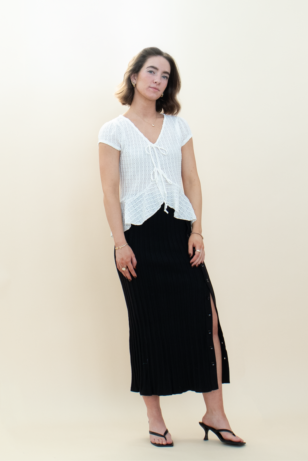 Woman wearing a white textured tie-front blouse with short sleeves and a black ribbed maxi skirt with side buttons from Groove Closet.