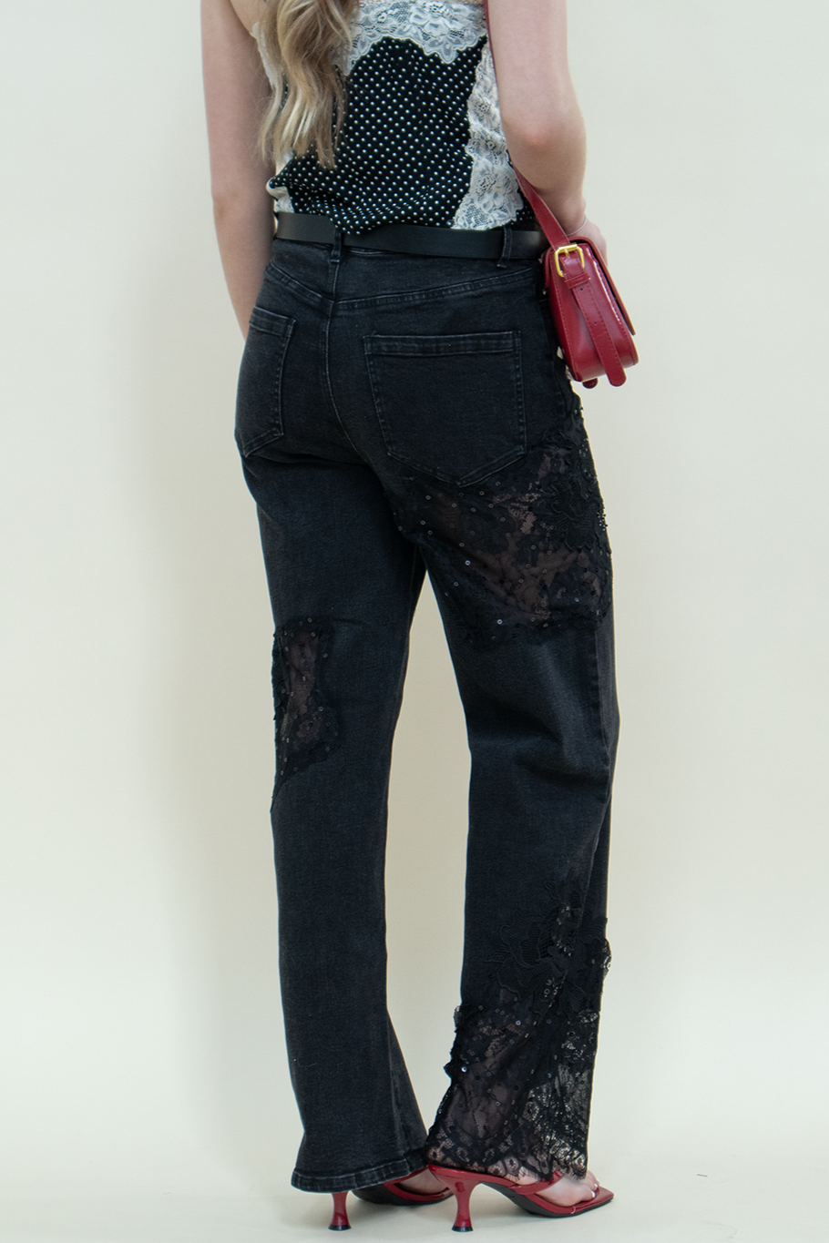 Close-up of black straight-leg jeans with sheer lace detailing and red kitten heels from Groove Closet.