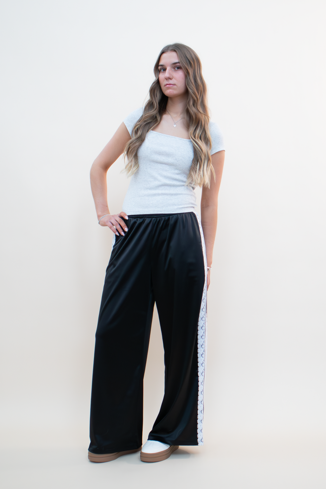 Woman modeling wide-leg black athletic pants with white lace side panels, styled with a fitted heather gray square-neck top—modern loungewear outfit for women ages 18–40 who love stylish and comfortable fashion.