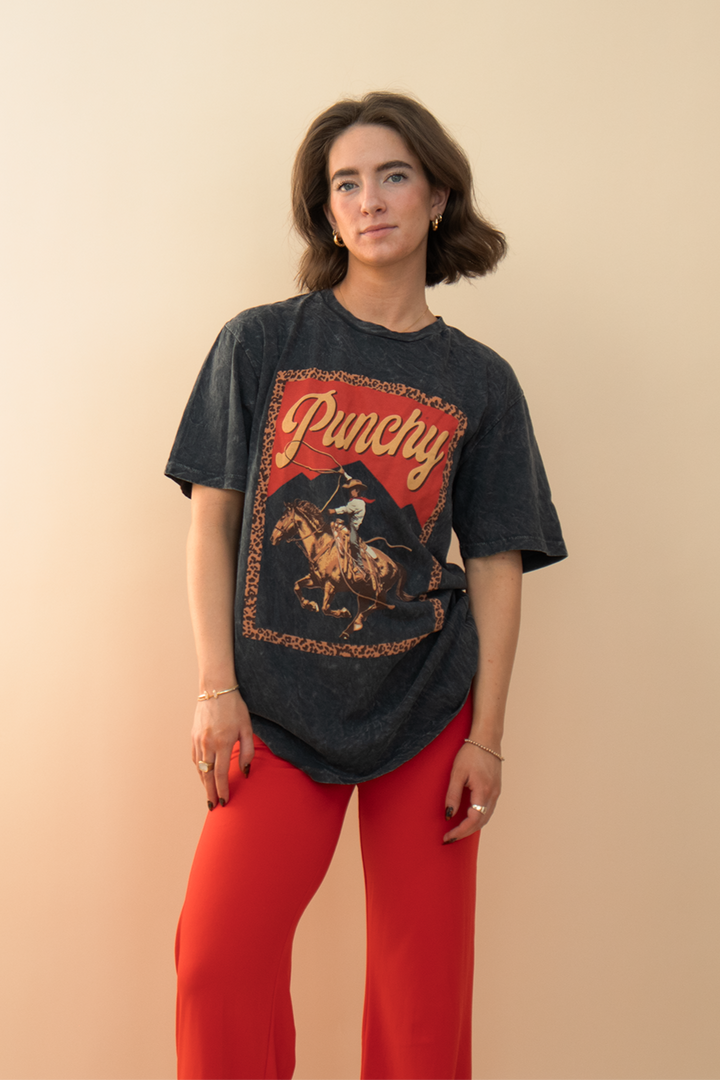 black cowboy graphic tee with the phrase "punchy" printed on it, styled with red pants.