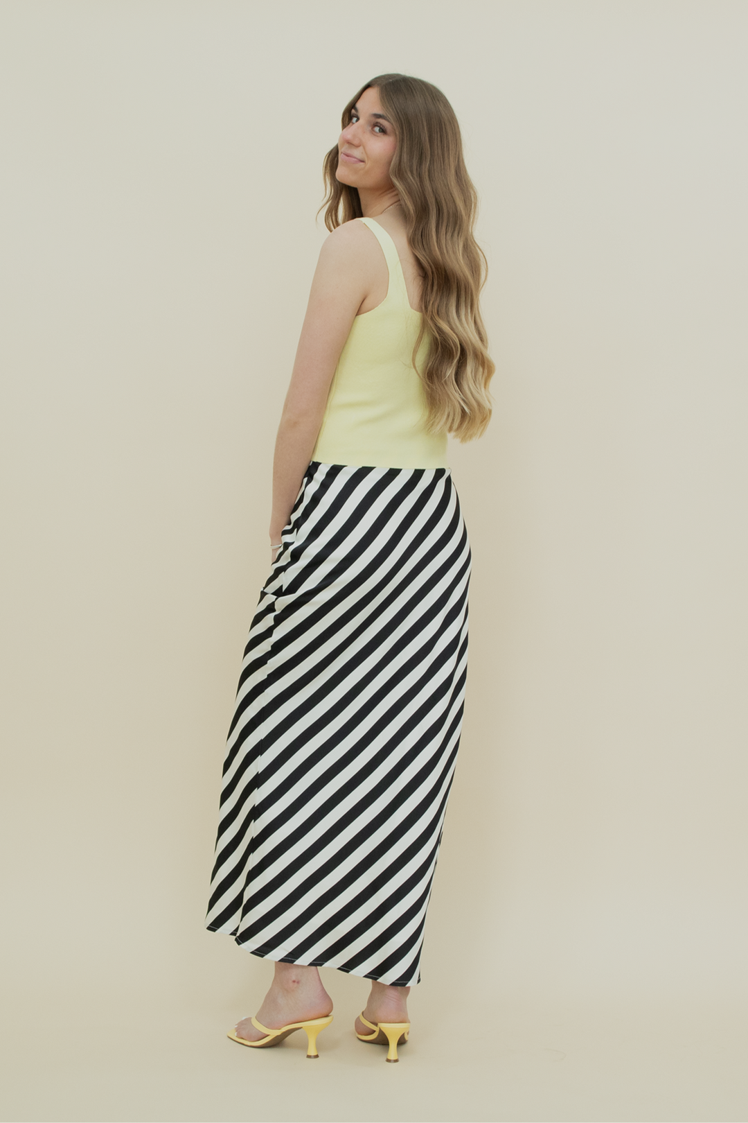 Back view of a black and white diagonal striped midi skirt with a sleek satin finish, designed for a flattering silhouette and bold summer style.