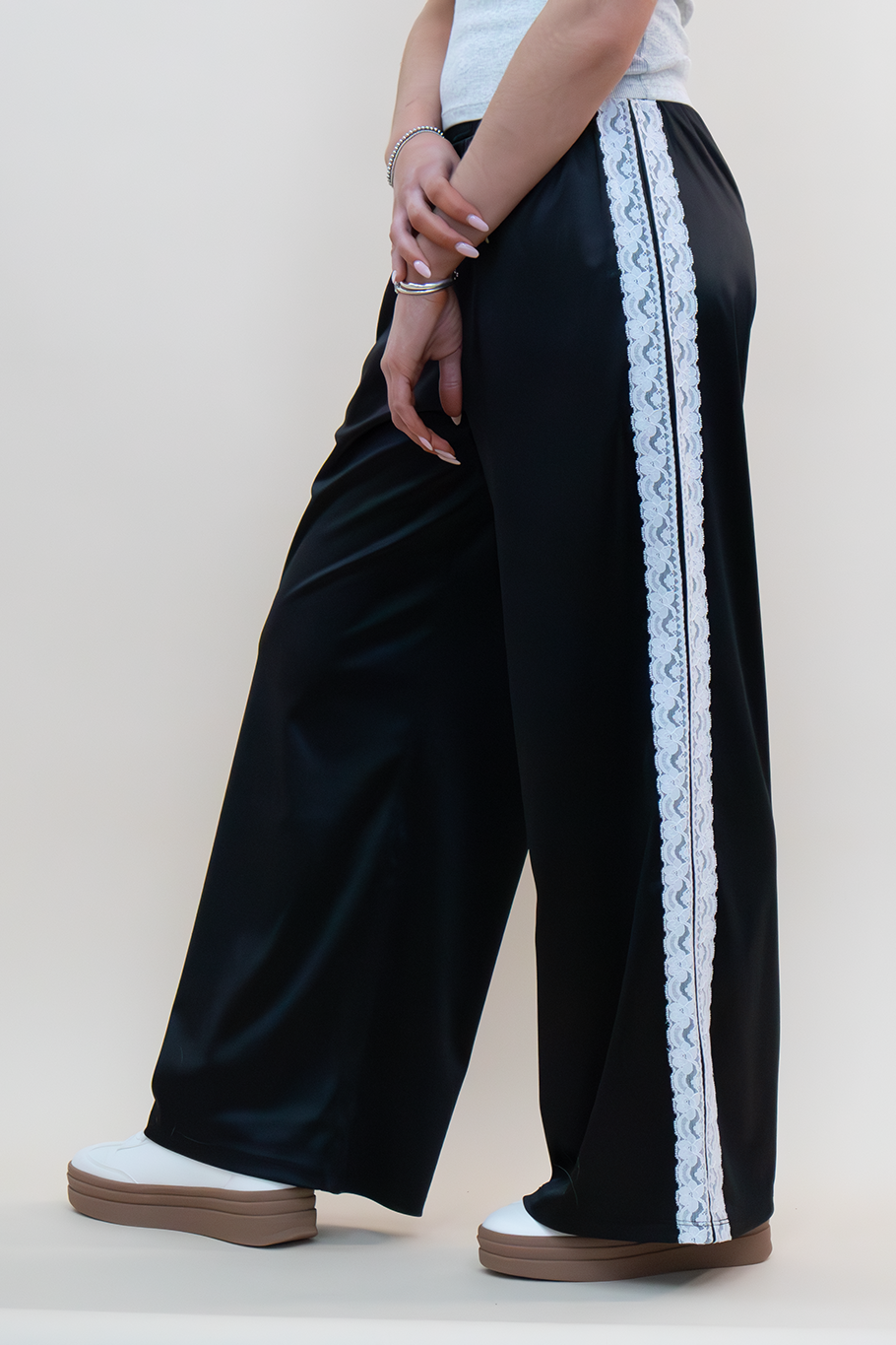 Close-up of black wide-leg lounge pants featuring a delicate white lace stripe down the sides, styled with a fitted heather gray top and platform sneakers—perfect for trendy women ages 18–40 seeking elevated casualwear.
