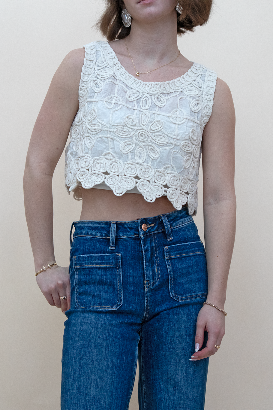 A zoomed in view of blue jean pockets, styled with an ivory floral tank.