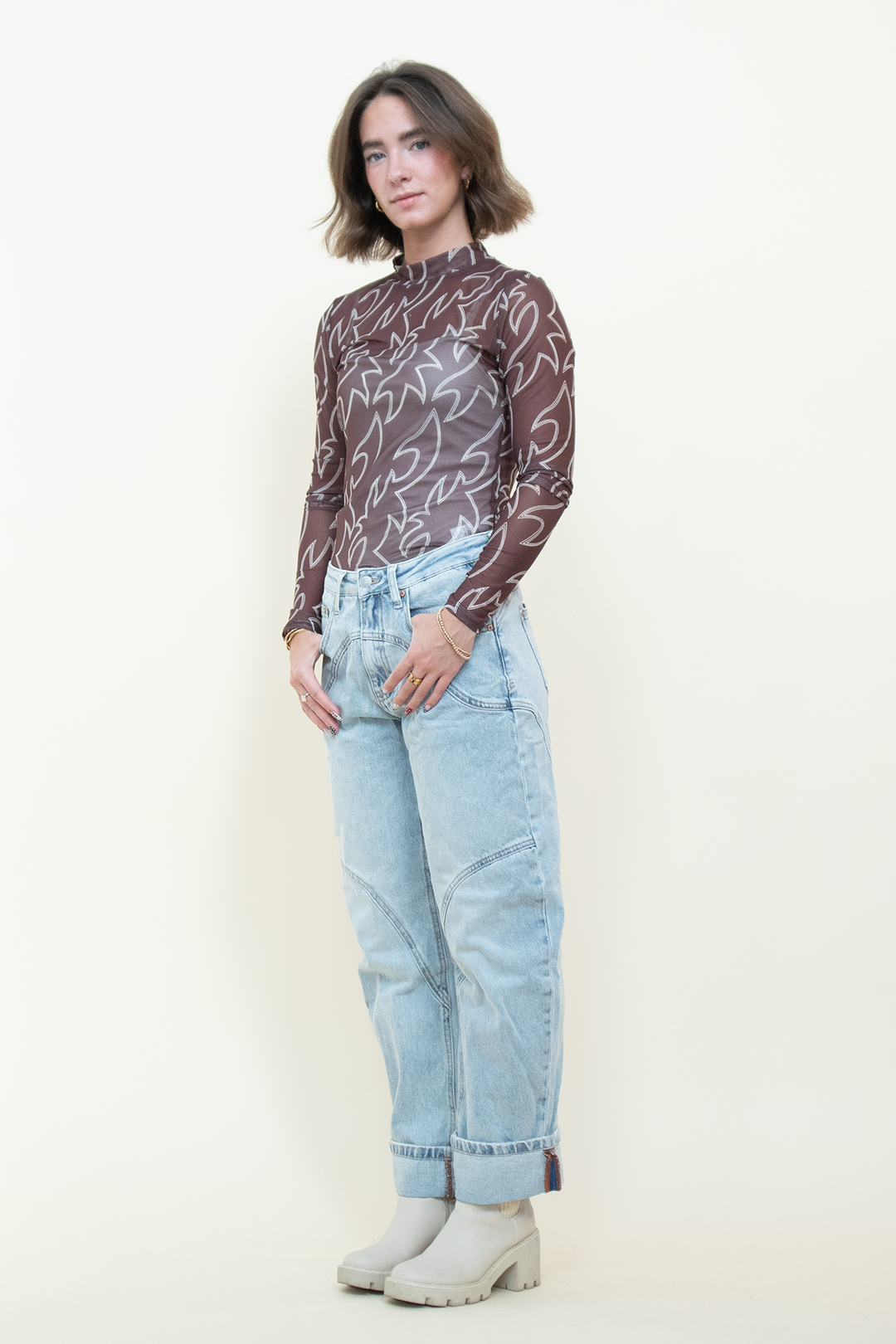 Model wearing a sheer brown mesh mock-neck top with white cami underneath, a cream Western-inspired abstract print and long fitted sleeves.