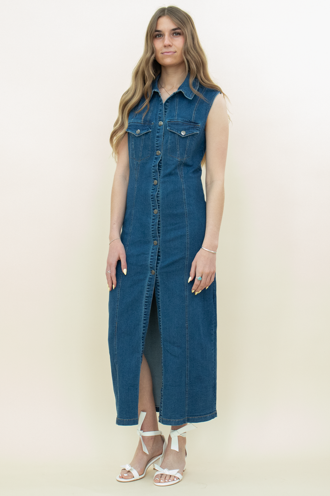 Sleeveless button-up denim midi dress with front slit, styled with white bow-tie sandals. Casual and chic fall outfit for women.
