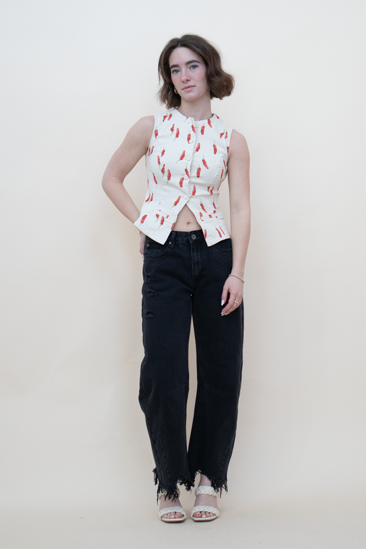 Sleeveless cream denim blouse with red pepper print styled on model wearing black distressed wide-leg jeans and braided heels — bold and playful summer top for casual women’s outfits.