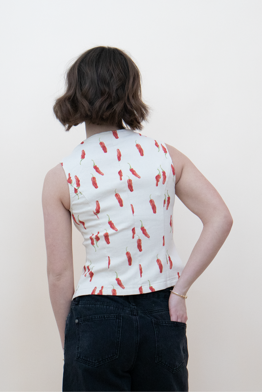 Back view of a sleeveless white top with red chili pepper print, fitted silhouette paired with high-waisted black jeans — bold summer blouse for women’s casual street style.