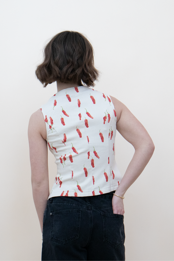 Back view of a sleeveless white top with red chili pepper print, fitted silhouette paired with high-waisted black jeans — bold summer blouse for women’s casual street style.