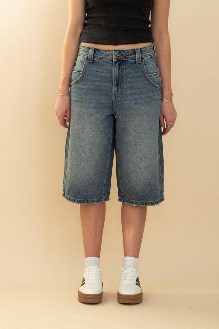 long denim jort in gray blue washed color, styled with a white sneaker and black top
