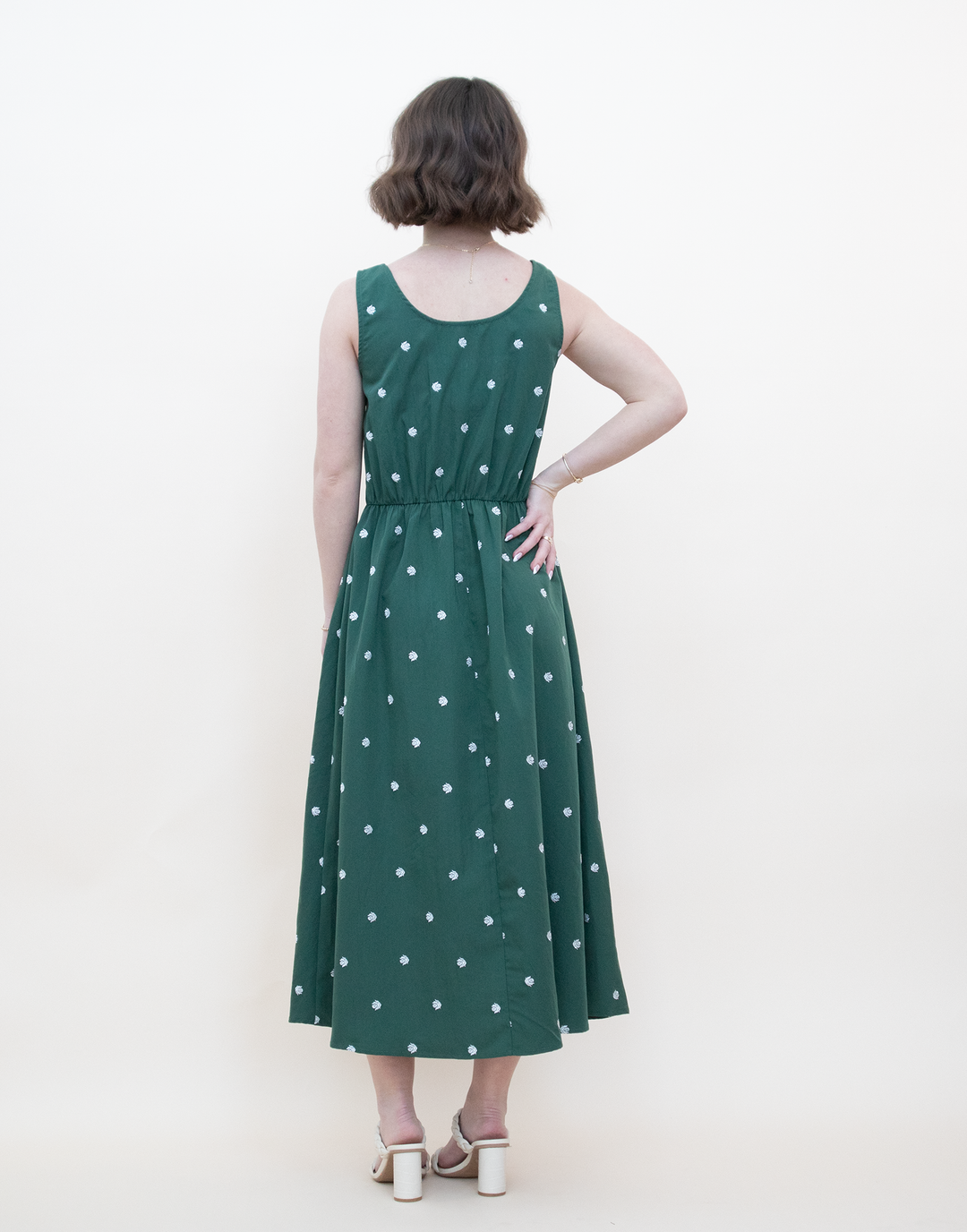 Back view of a women's dark green daisy print sleeveless midi dress with a relaxed A-line fit and tiered skirt detail