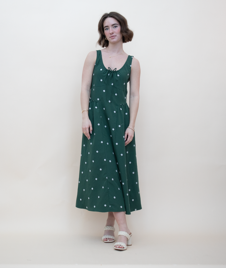 Women's dark green sleeveless midi dress with white daisy floral print, gathered tie neckline, and A-line silhouette, styled with cream block heel sandals