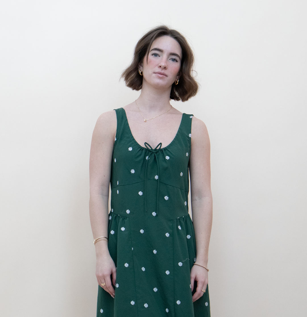 Close-up of a women's dark green floral midi dress featuring a scooped neckline with a delicate tie closure and white daisy embroidered print detail