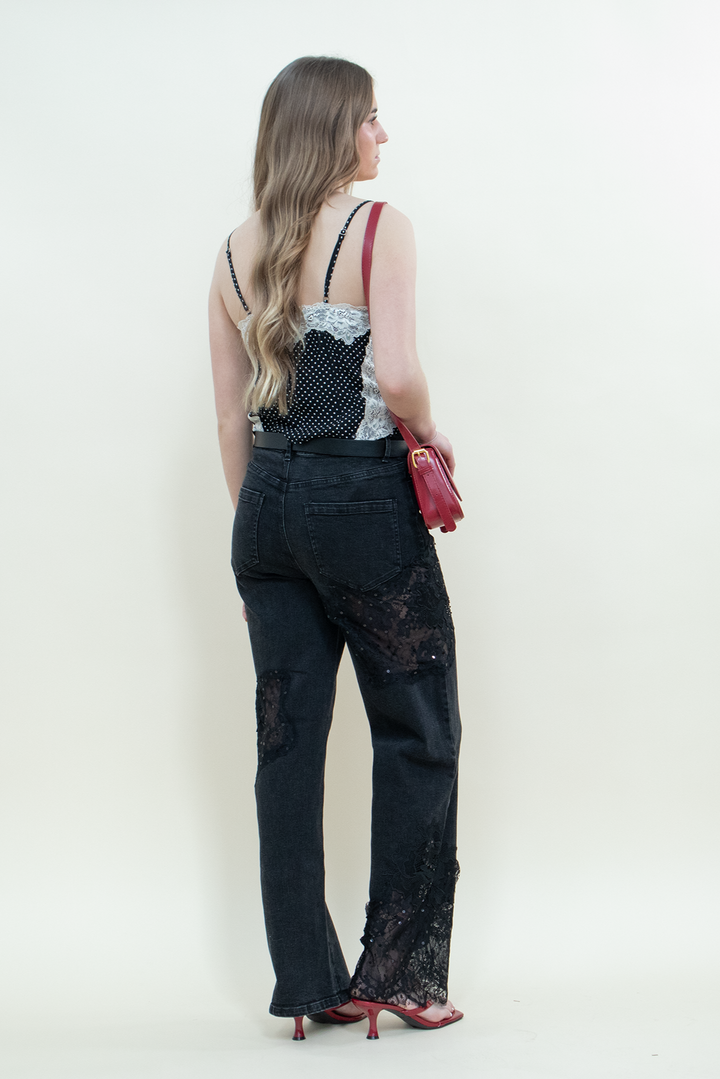Model facing away in black straight-leg jeans with sheer lace panels from Groove Closet, paired with a black polka dot camisole with white lace trim, red handbag, and red kitten heels.