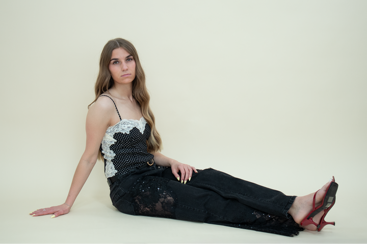 Model sitting on the floor wearing black lace-panel straight-leg jeans from Groove Closet, paired with a black polka dot camisole with white lace trim and red kitten heel sandals.