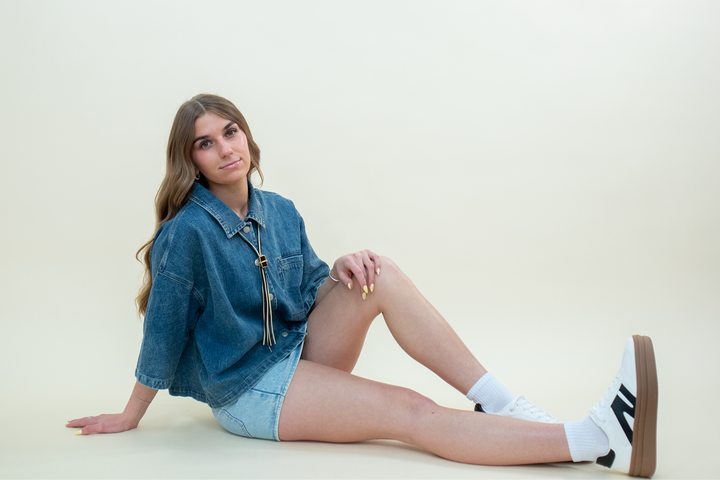 Model sitting on floor wearing oversized denim jacket with light wash mini skirt and white sneakers, styled by Groove Closet.