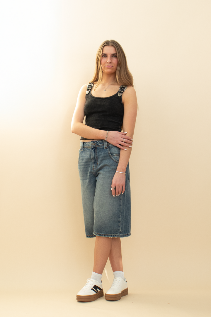 long denim short that goes past the knee, styled with a black tank and white sneaker