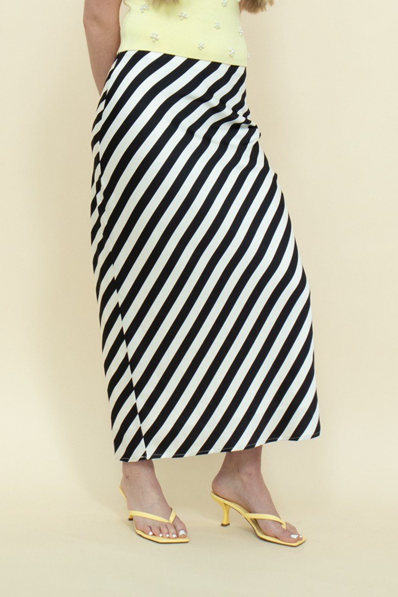 Detail shot of a bold striped midi skirt in black and white paired with minimalist yellow heels—statement summer look combining modern edge with playful color contrast.