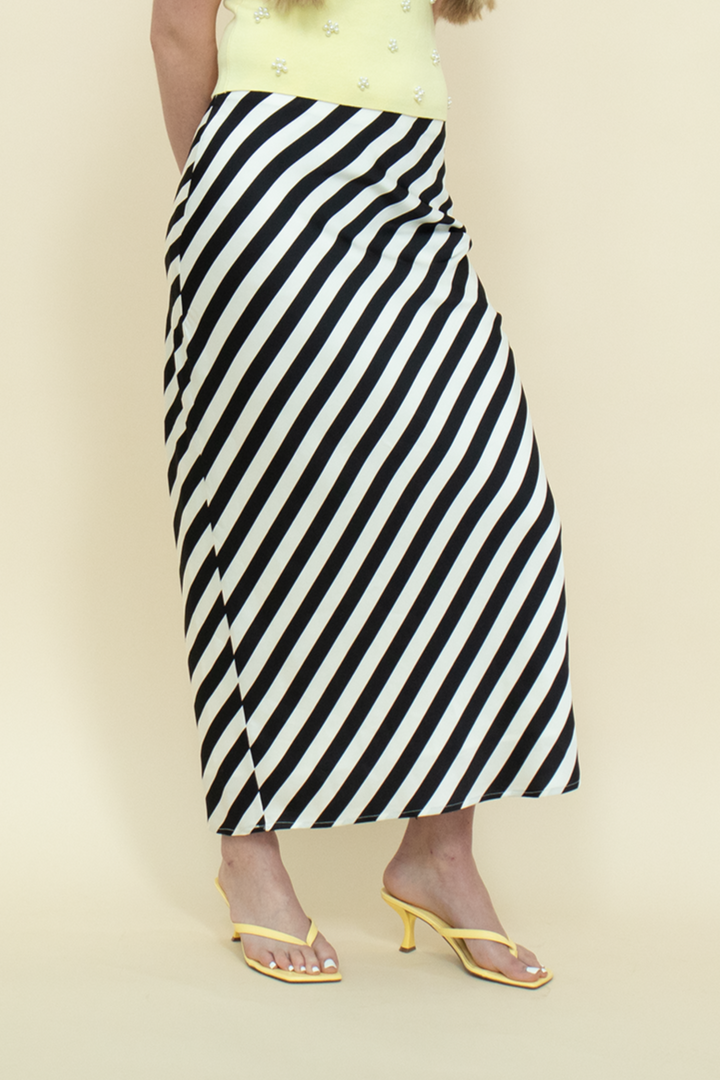 Detail shot of a bold striped midi skirt in black and white paired with minimalist yellow heels—statement summer look combining modern edge with playful color contrast.