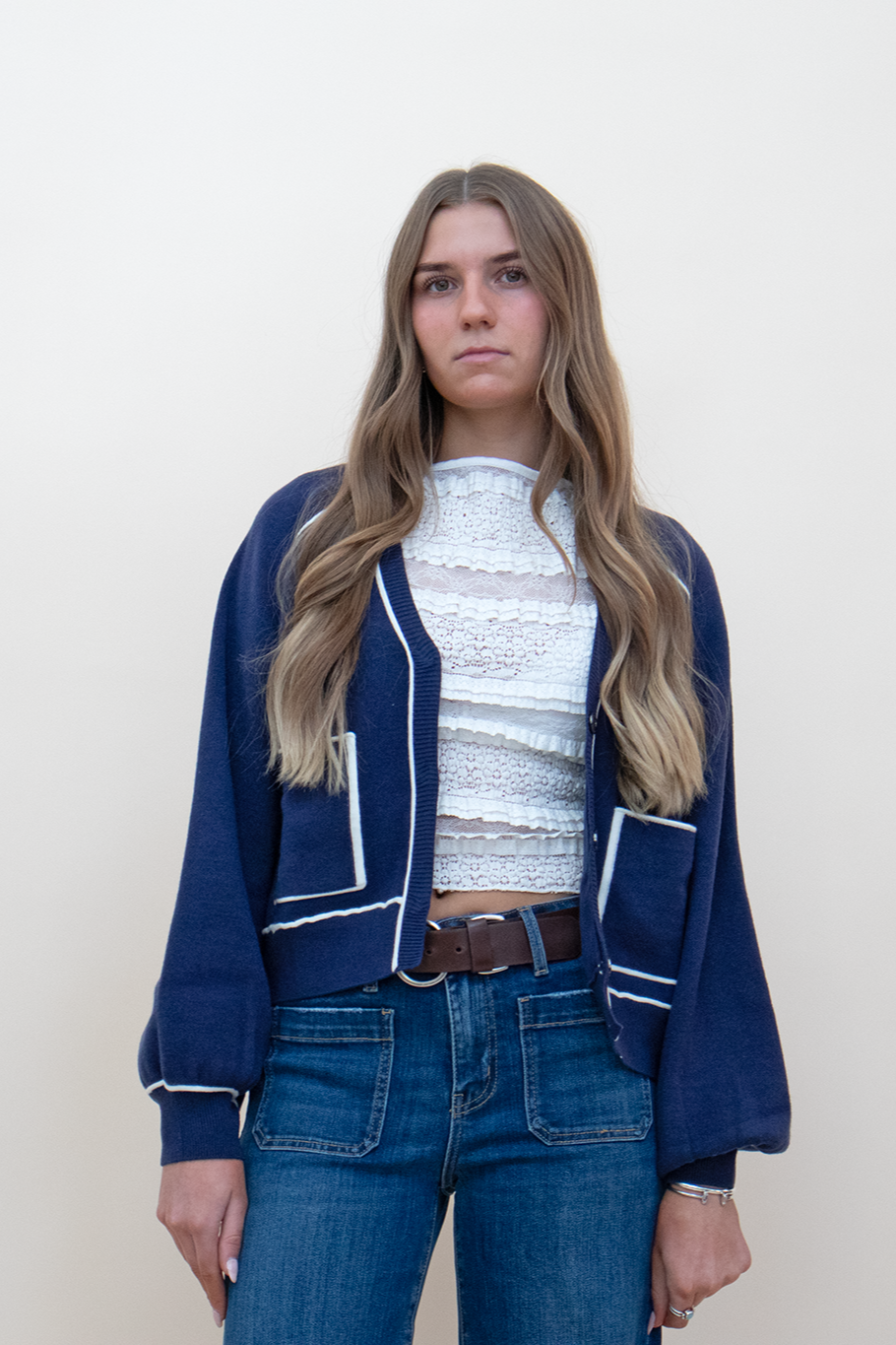 navy blue cardigan with white line detailing, styled with a dark blue jean, white lace top, and brown belt.