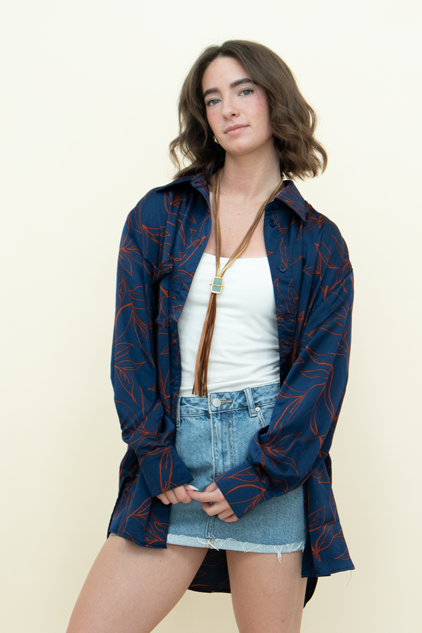 Woman wearing a navy blue oversized button up with a red leaf pattern, a bolo necklace, a white cami, and mini skirt. Perfect casual layering piece in a cool girl style. 