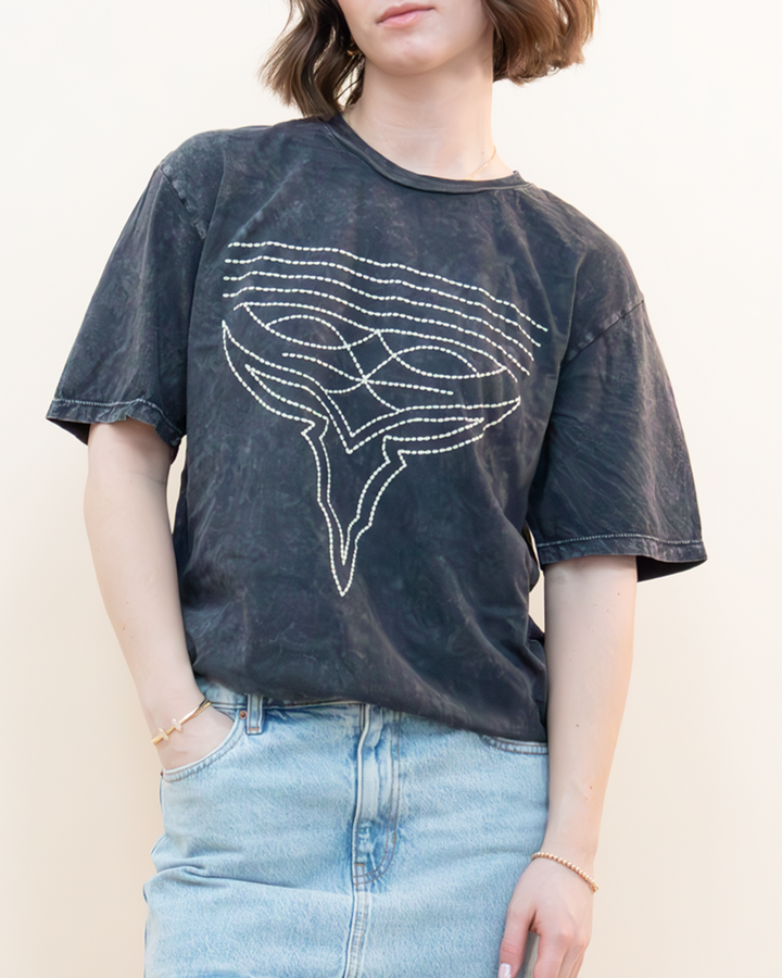 Close-up of a model in a relaxed fit washed black graphic tee paired with a high-waisted light denim skirt. Trendy vintage-inspired outfit styled for women seeking unique casual pieces, available at Groove Closet.