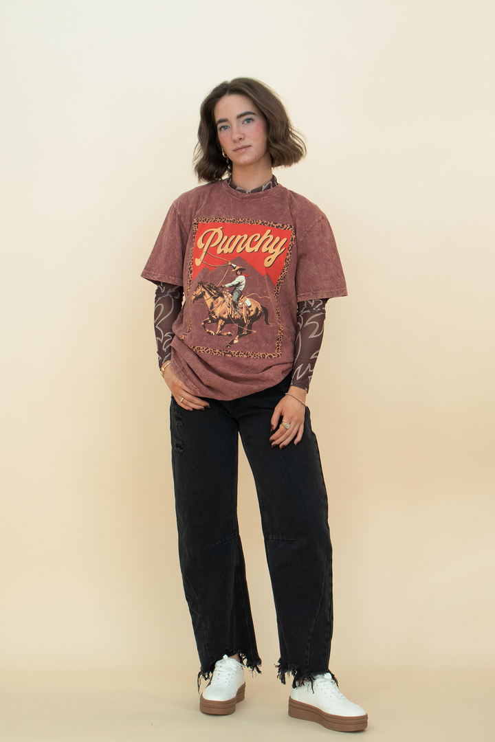 red-brown "punchy" graphic tee with a cowboy on it, styled with a black barrel jean and a white sneaker.