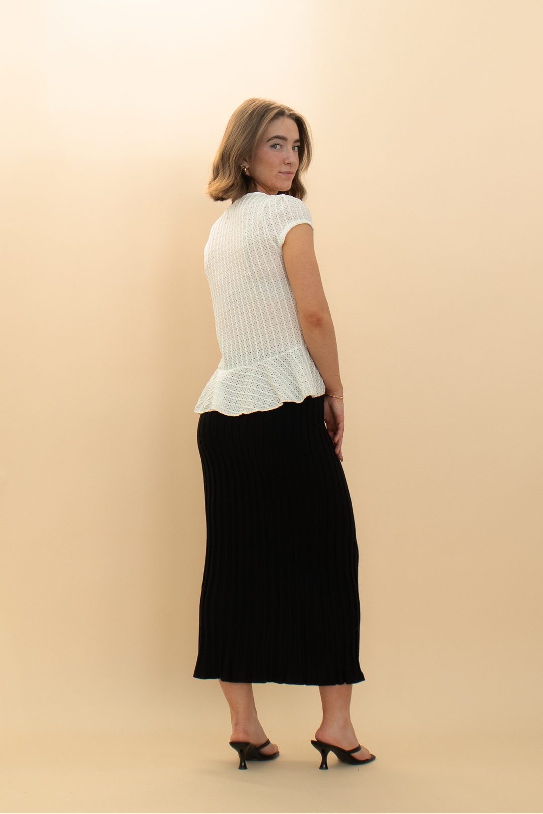 Back of a white cap sleeve eyelet peplum blouse featuring bow accents, styled with a fitted black pencil skirt for a trendy women's outfit.