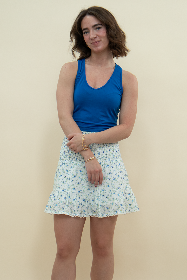 Smocked floral mini skirt with ruffle hem and delicate lace trim, styled with a vibrant royal blue tank top – feminine summer outfit idea for warm-weather wardrobes.