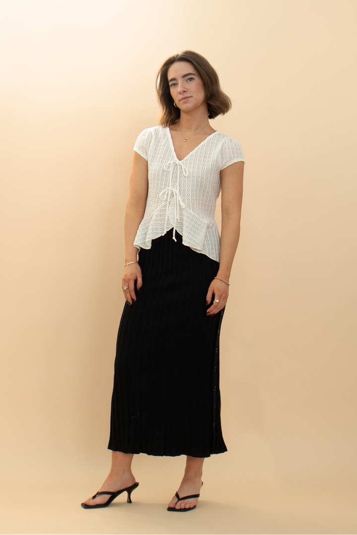 Trendy white eyelet peplum blouse with cap sleeves and bow details, paired with a sleek black pencil skirt for a stylish women's look.