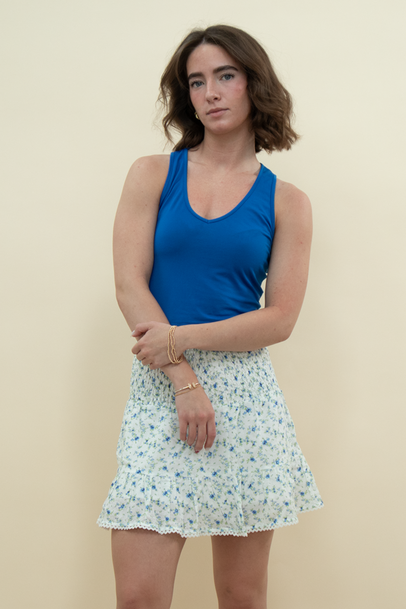 Model wearing a high-waisted white mini skirt with blue floral print and ruffled hem, styled with a bold blue tank top – perfect for a light, summery, vintage-inspired outfit.
