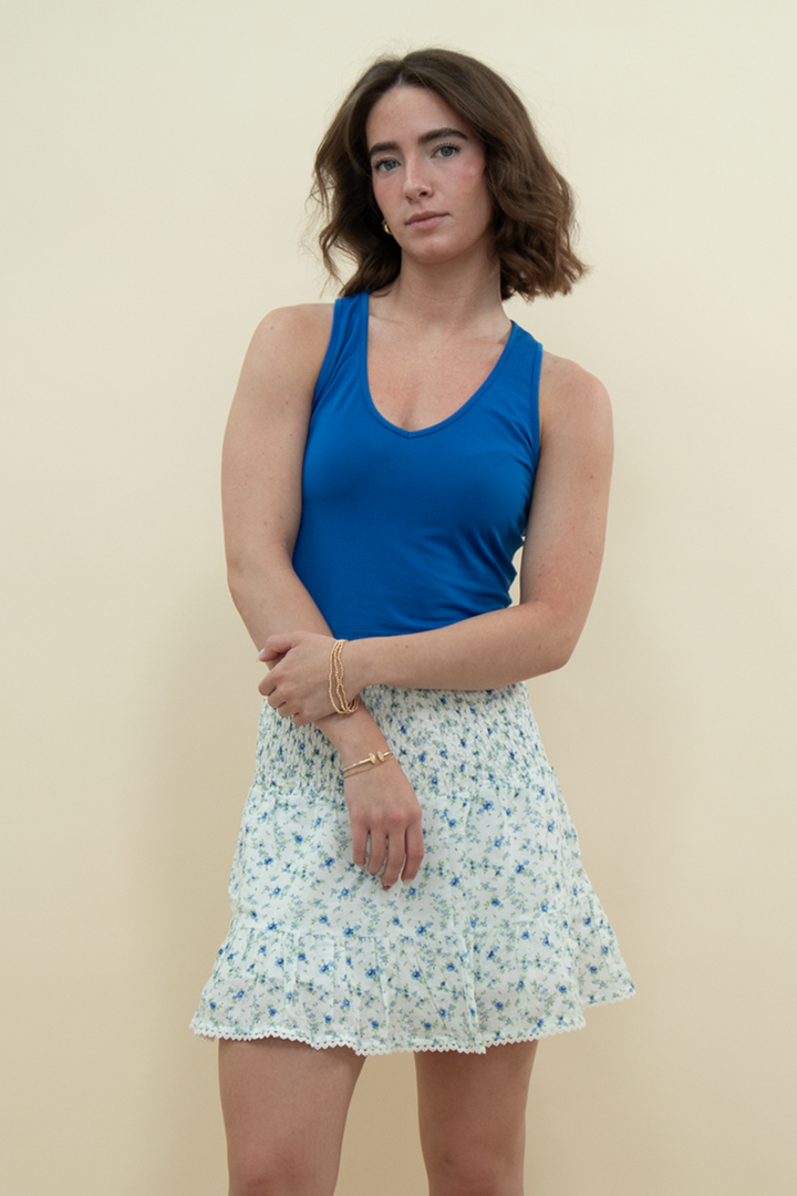 Model wearing a high-waisted white mini skirt with blue floral print and ruffled hem, styled with a bold blue tank top – perfect for a light, summery, vintage-inspired outfit.