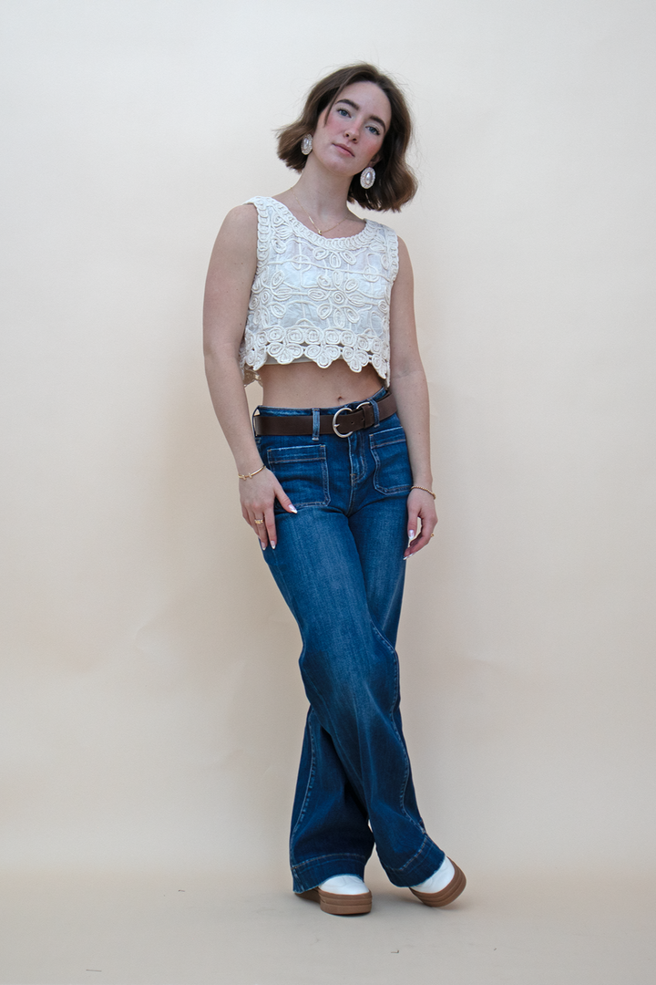 wide leg blue jeans styled with white sneakers, an ivory cropped tank top, and a brown belt

