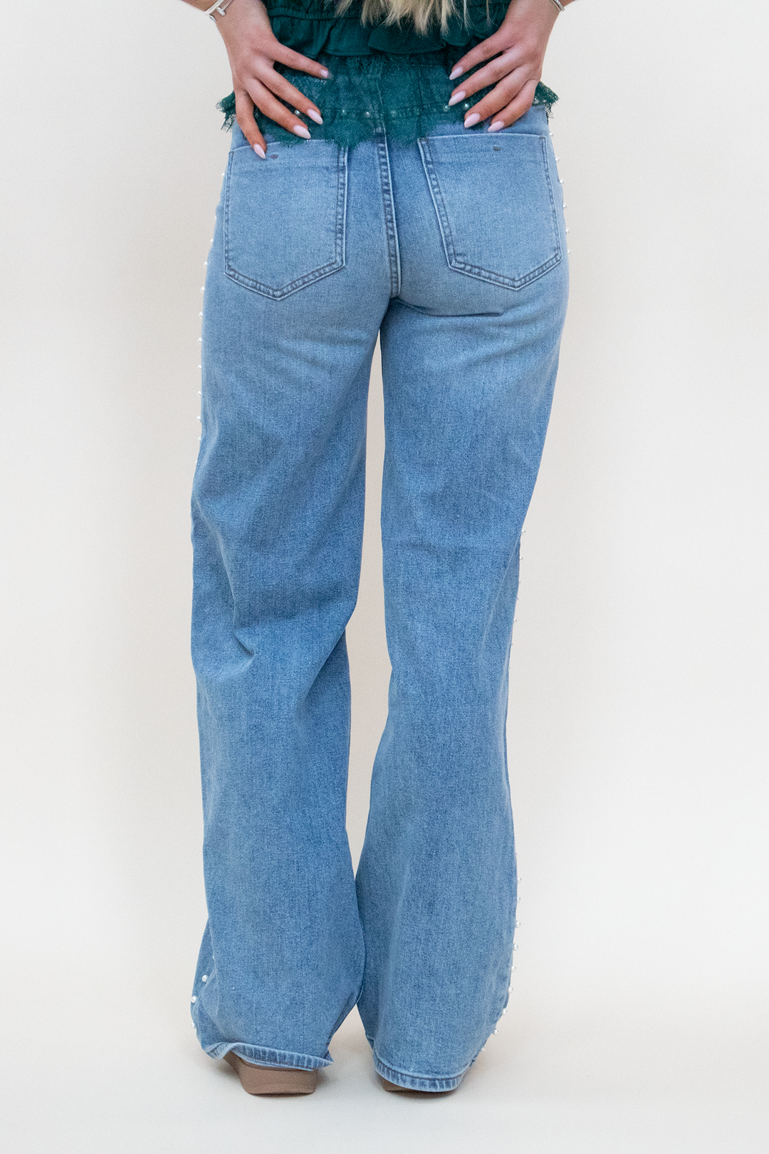 Back view of light wash wide-leg flare jeans with classic double back pockets, subtle flare silhouette, and pearl stud side seam detail visible at the hem