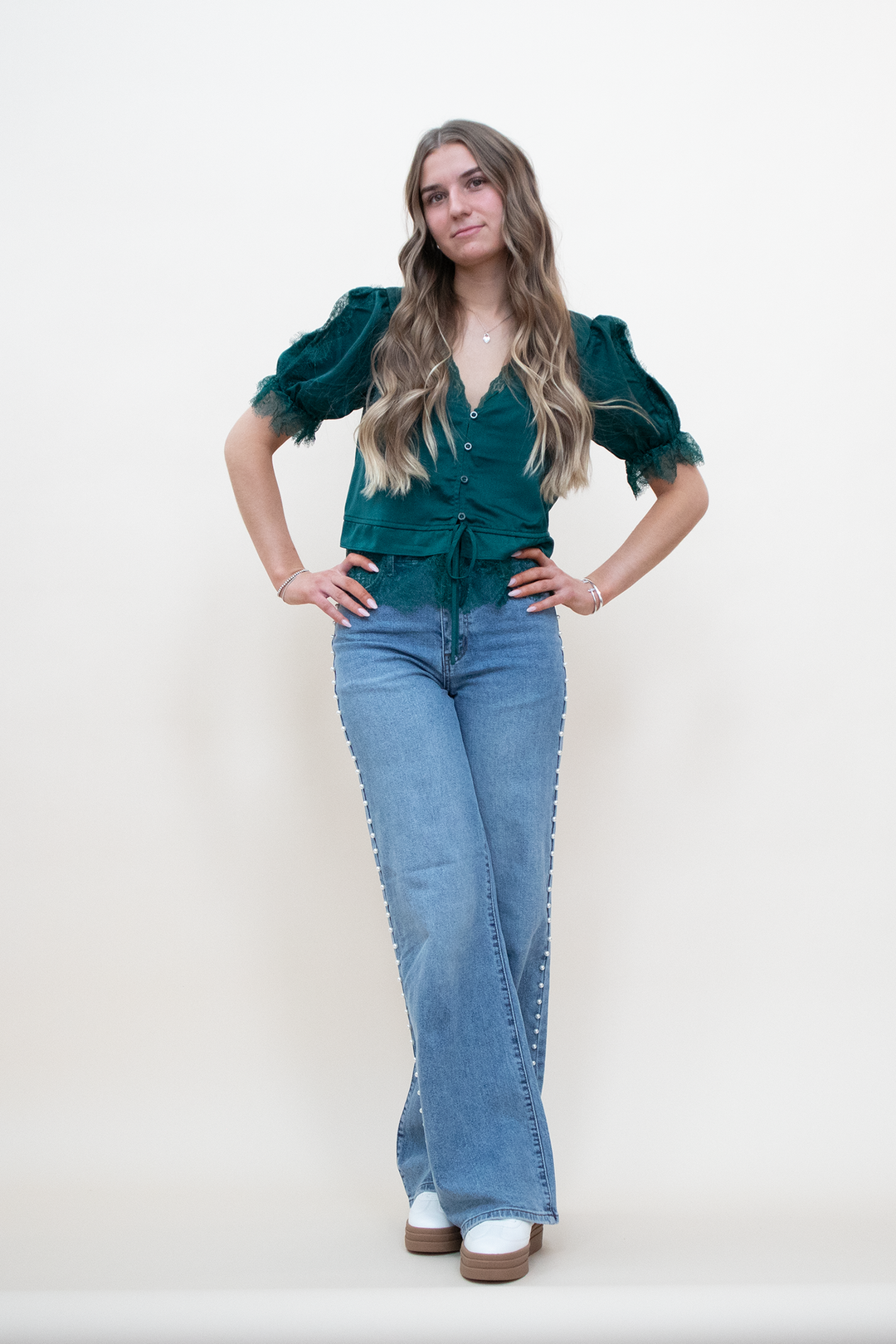 Light wash wide-leg flare jeans featuring a double pearl stud stripe down the outer seam, high-rise waist, front-facing view on model with hands on hips