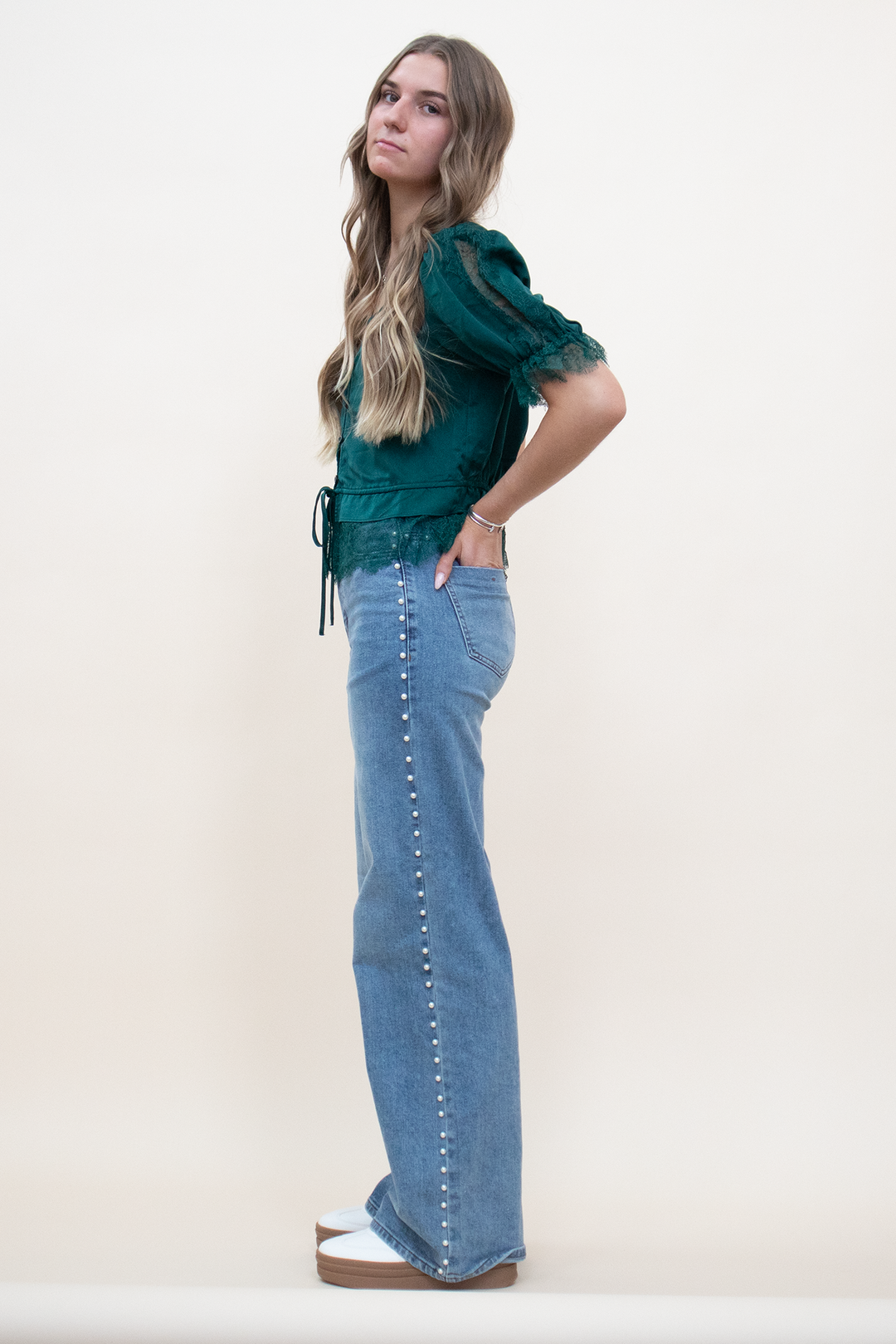 Side view of high-rise light wash wide-leg flare jeans with continuous pearl stud embellishment running the full length of the outer seam from hip to hem