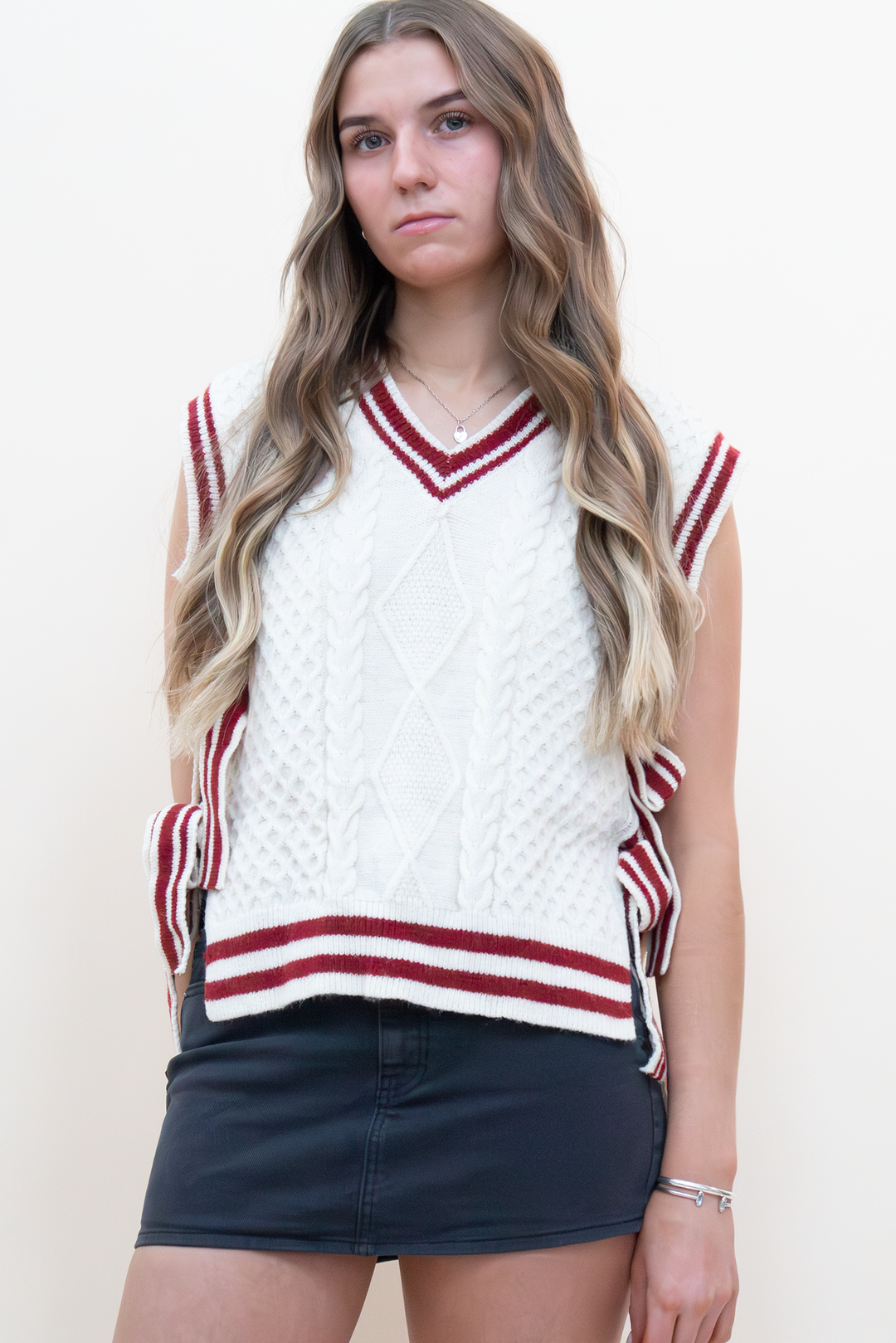 Cream cable knit sweater vest with burgundy varsity stripe trim and V-neckline, styled with a dark denim mini skirt