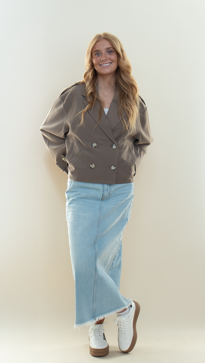 Taupe cropped trench jacket worn open over a white tank top with a light wash denim maxi skirt and white platform sneakers