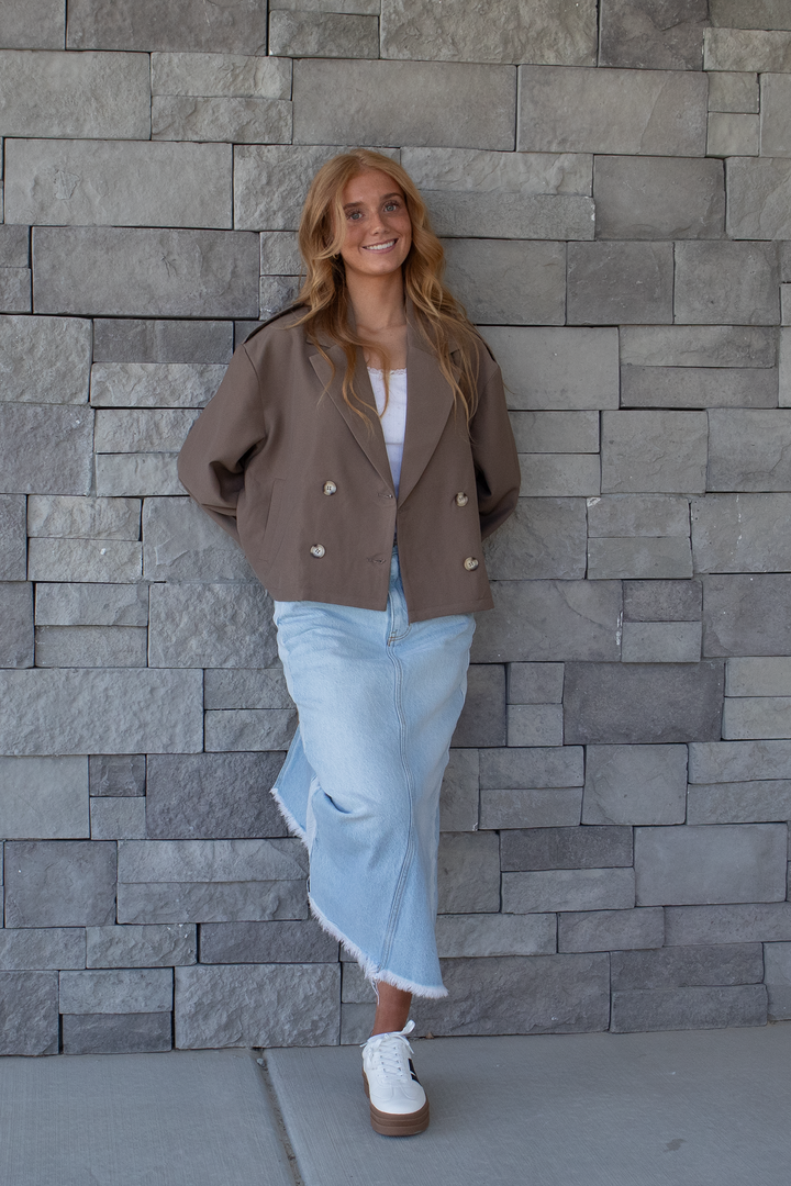 Taupe cropped double breasted trench jacket styled with a frayed hem denim maxi skirt, white platform sneakers, and white tank top