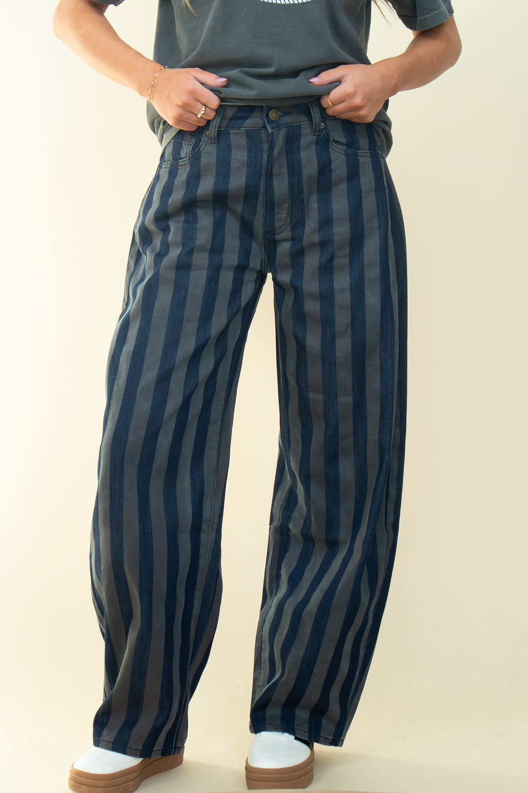 Close-up front view of dark-wash and gray vertically striped jeans showing the waistband, front pockets, and relaxed wide-leg silhouette.