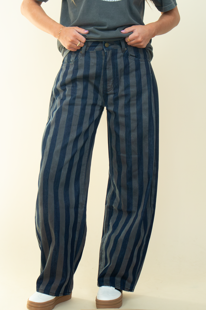 Close-up front view of dark-wash and gray vertically striped jeans showing the waistband, front pockets, and relaxed wide-leg silhouette.