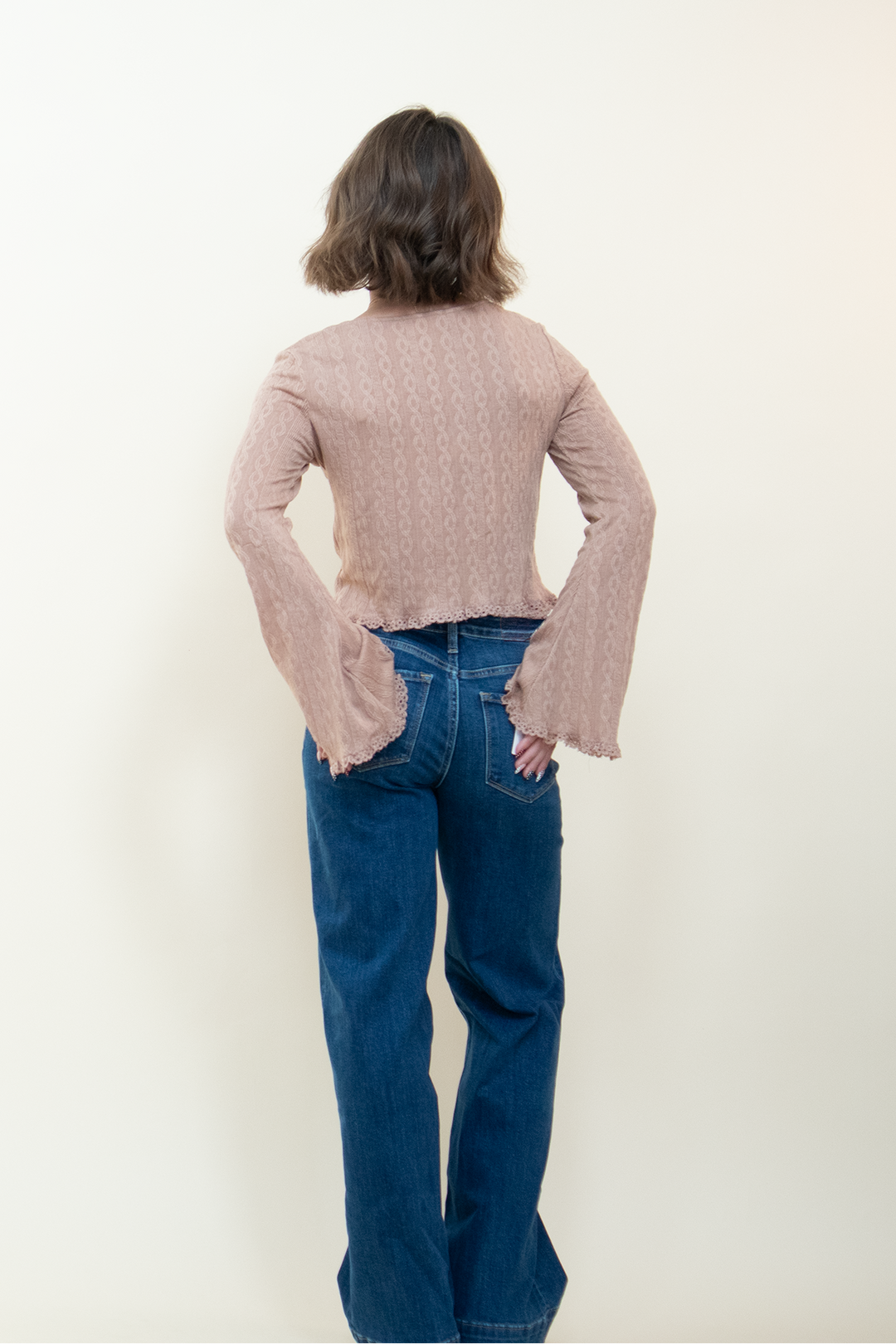 Back view of dusty pink long sleeve crop top with bell sleeves and lace hem trim, paired with wide leg blue jeans