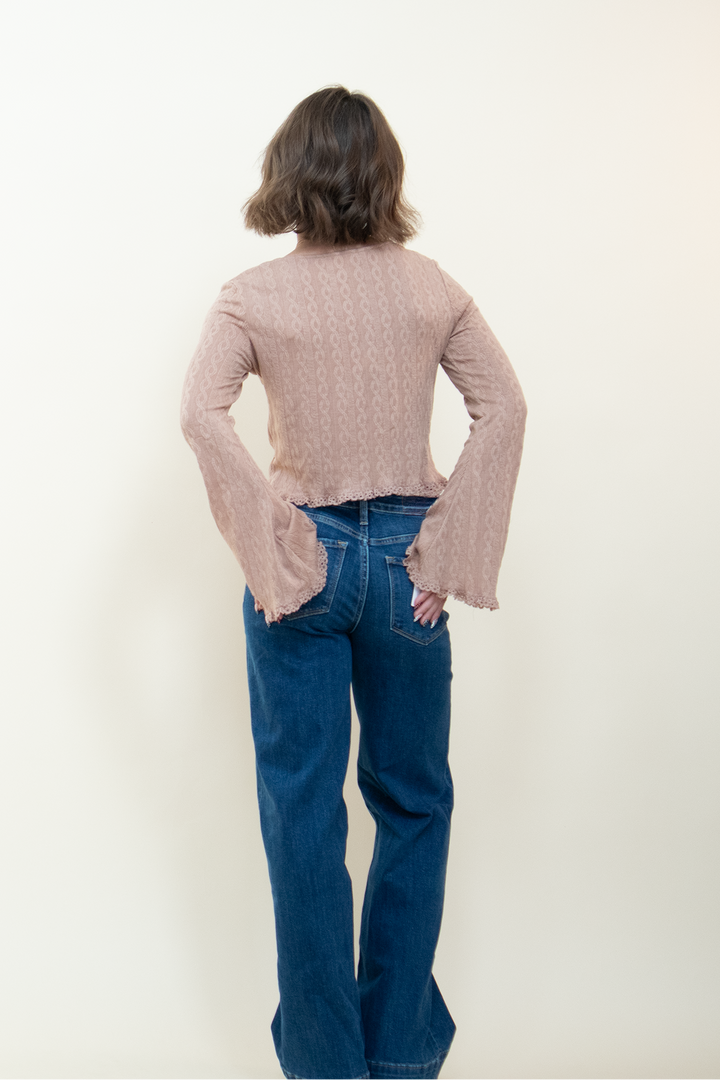Back view of dusty pink long sleeve crop top with bell sleeves and lace hem trim, paired with wide leg blue jeans