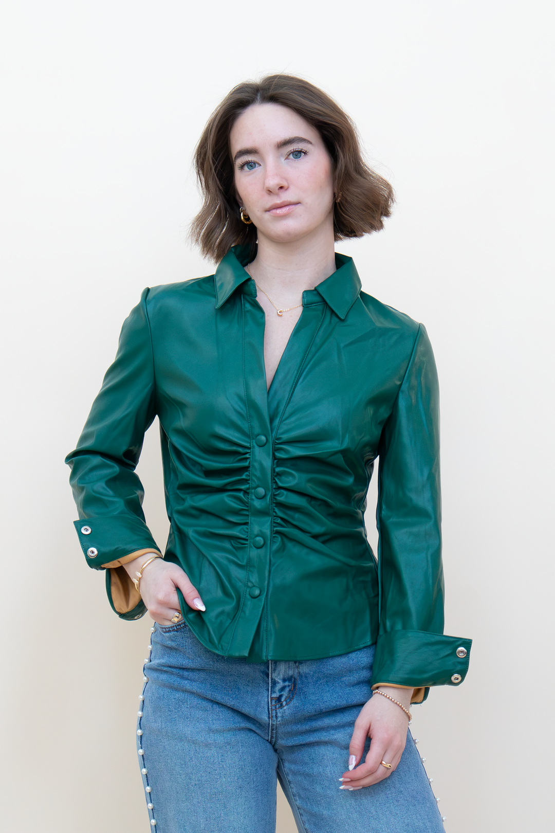 Front view of emerald green leather-look blouse with a collared neckline, covered buttons, ruched waist, and button cuffs.