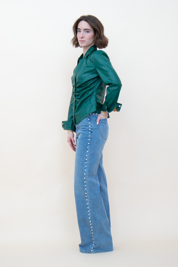Side view of emerald green ruched leather-look blouse showing its fitted waist, collared neckline, and curved hem.